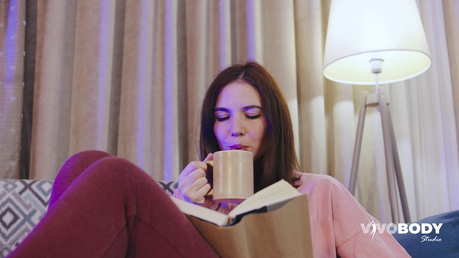 Woman relaxing on a sofa at home with a book and a mug of tea